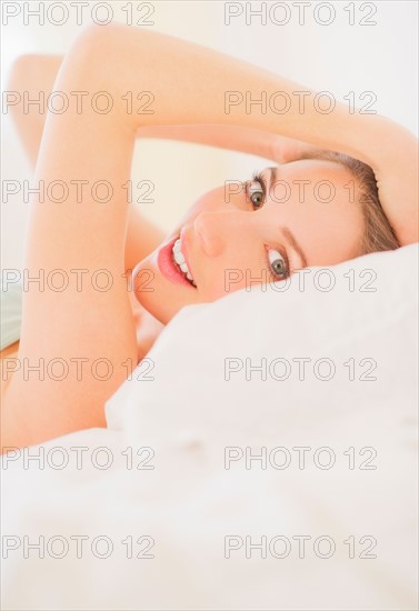 Portrait of young woman lying on bed in bedroom. Photo : Daniel Grill