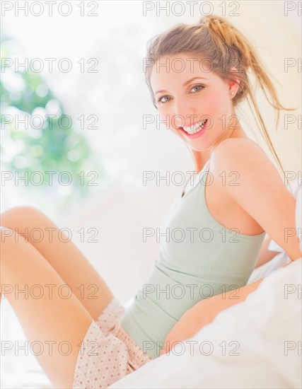 Portrait of young woman lying on bed in bedroom. Photo : Daniel Grill