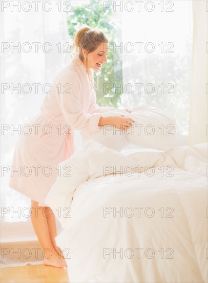 Portrait of young woman making bed. Photo : Daniel Grill