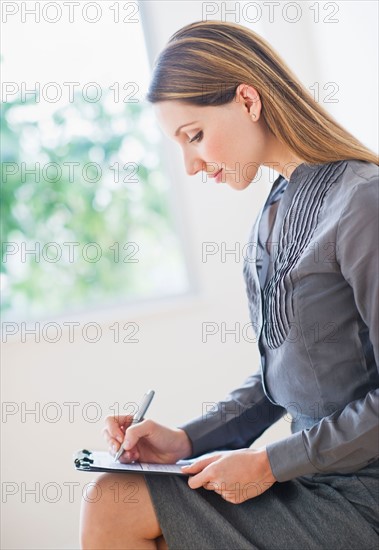 Side view of young business woman sitting and making notes. Photo : Daniel Grill