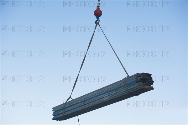 Mid-air view at crane's hook lifting wooden planks. Photo : fotog