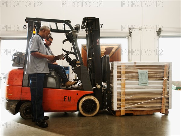 Warehouse workers talking by forklift truck.