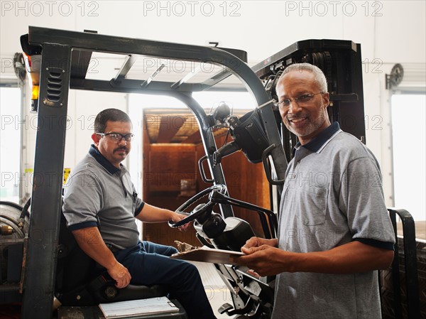 Portrait of warehouse workers by forklift truck.