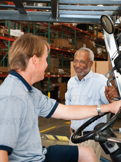 Businessman talking to forklift driver in warehouse.