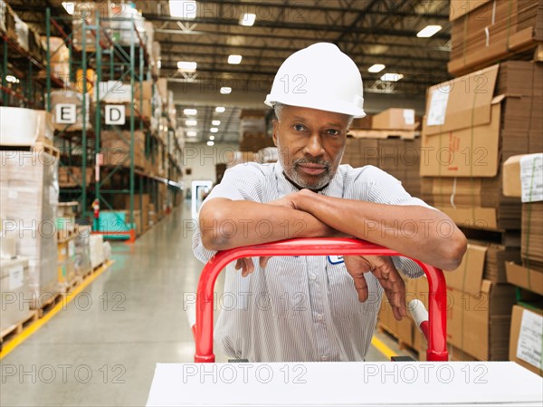 Portrait of man pushing hand truck in warehouse.