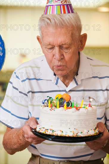 Senior man blowing candles on birthday cake.