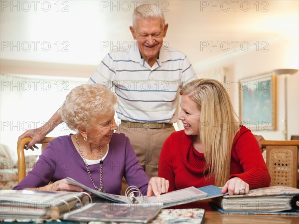 Senior couple and mid adult woman watching family scrapbooks.