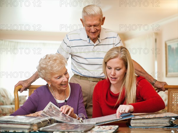 Senior couple and mid adult woman watching family scrapbooks.