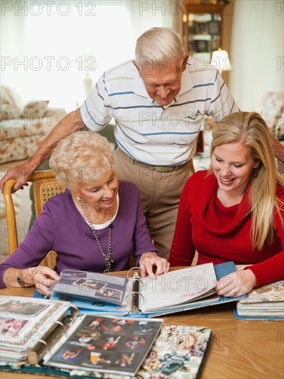 Senior couple and mid adult woman watching family scrapbooks.