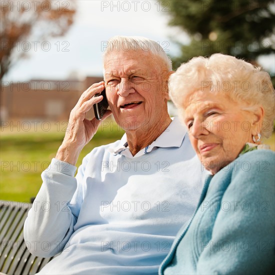 Senior woman with man using phone in park.