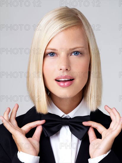 Studio portrait of young waitress adjusting bow tie. Photo : Yuri Arcurs