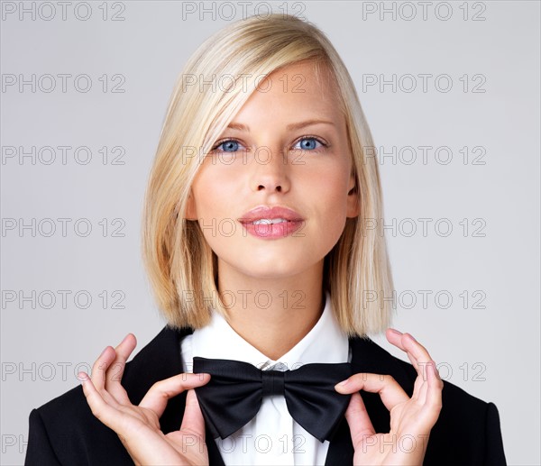 Studio portrait of young waitress adjusting bow tie. Photo : Yuri Arcurs