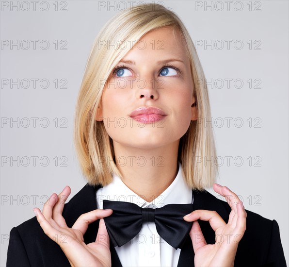 Studio portrait of young waitress adjusting bow tie. Photo : Yuri Arcurs