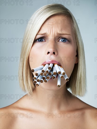 Studio portrait of young woman with mouthful of cigarettes. Photo : Yuri Arcurs