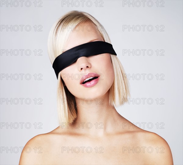 Young woman wearing blindfold, studio shot. Photo : Yuri Arcurs