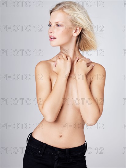 Young shirtless woman with arms covering breasts, studio shot. Photo : Yuri Arcurs