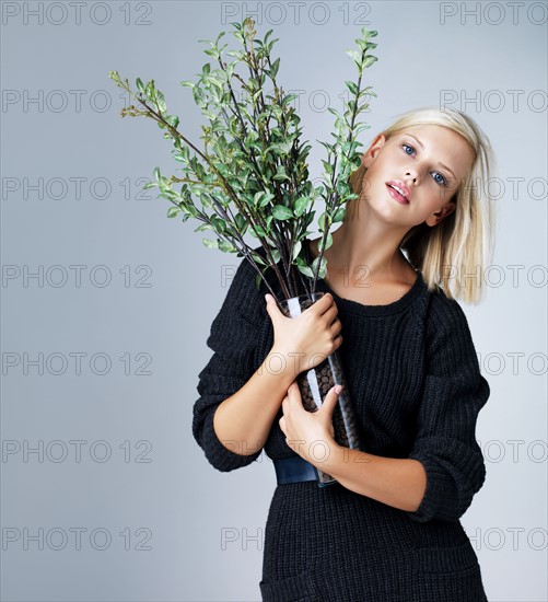 Young woman holding vase with green twigs, studio shot. Photo : Yuri Arcurs