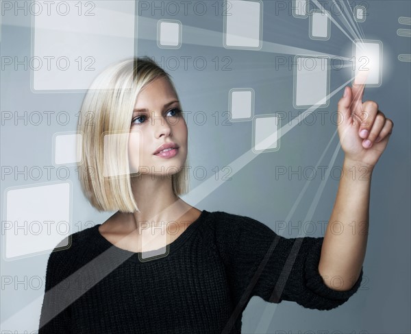 Young woman using futuristic touchscreen, studio shot. Photo : Yuri Arcurs