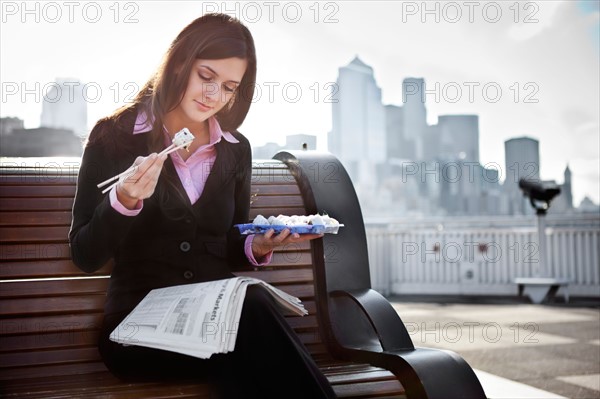 USA, Seattle, Young businesswoman eating sushi and reading newspaper. Photo : Take A Pix Media