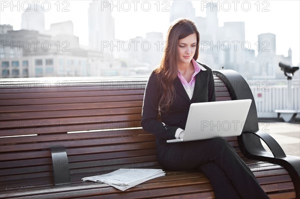USA, Seattle, Young businesswoman working on laptop on bench. Photo : Take A Pix Media