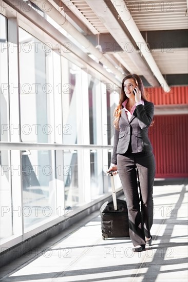 Smiling businesswoman walking with suitcase. Photo : Take A Pix Media