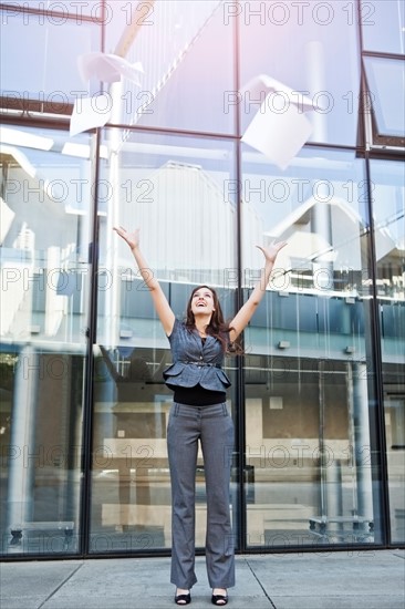 USA, Seattle, Young businesswoman throwing documents in front of office building. Photo : Take A Pix Media
