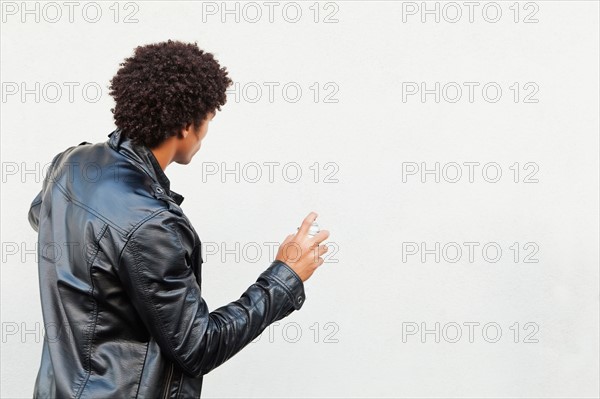 Man holding spray paint against white wall, studio shot. Photo : Sarah M. Golonka