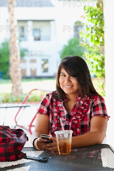 USA, California, La Quinta, Young woman using phone in outdoor cafe. Photo : Sarah M. Golonka