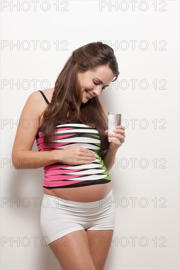 Portrait of pregnant woman holding glass of water, studio shot. Photo : Jan Scherders