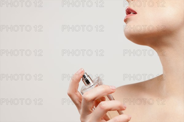 Close up of beautiful young woman spraying perfumes, studio shot. Photo : Jan Scherders