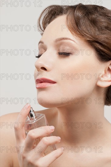 Portrait of beautiful young woman spraying perfumes, studio shot. Photo : Jan Scherders