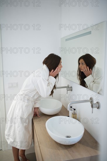 Tired woman looking in bathroom mirror. Photo : Mark de Leeuw