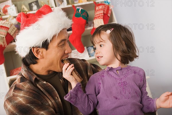 Girl feeding father wearing santa hat. Photo : Rob Lewine