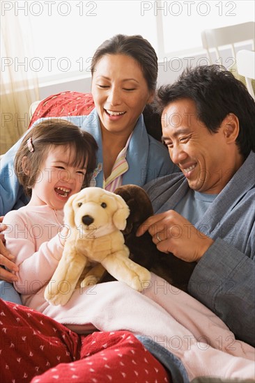 Parents and daughter sitting in bed and playing with stuffed toys. Photo : Rob Lewine