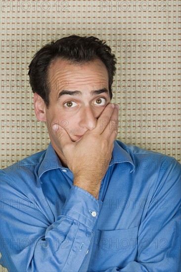 Studio portrait of mid adult man covering mouth with hand. Photo : Rob Lewine