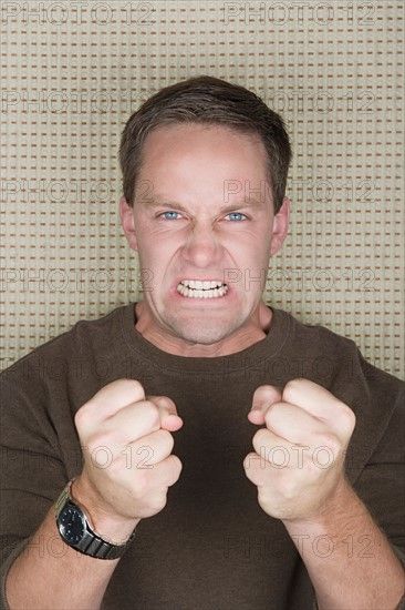 Studio portrait of mature man clenching teeth and fists. Photo : Rob Lewine