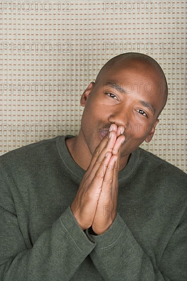 Studio portrait of mid adult man with hands clasped over mouth. Photo : Rob Lewine