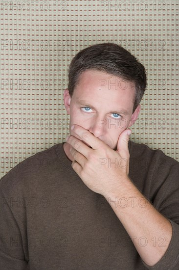 Studio portrait of mature man covering mouth with hand. Photo : Rob Lewine