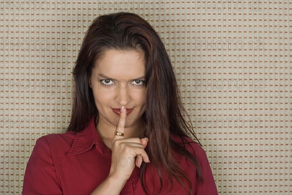 Studio portrait of mid adult woman with finger on lips. Photo : Rob Lewine