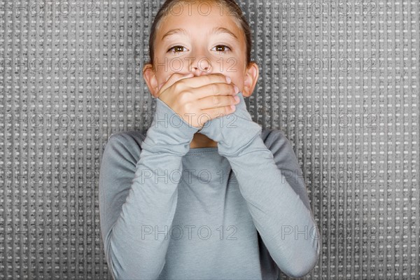 Studio portrait of girl (12-13) covering mouth with hands. Photo : Rob Lewine