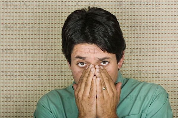 Studio portrait of mature man covering mouth with hands. Photo : Rob Lewine