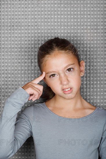 Studio portrait of teenage (12-13) girl touching forehead with finger. Photo : Rob Lewine