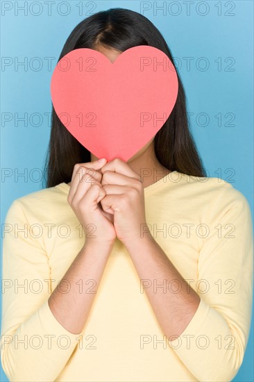 Studio portrait of teenage (16-17) girl holding paper heart over face. Photo : Rob Lewine