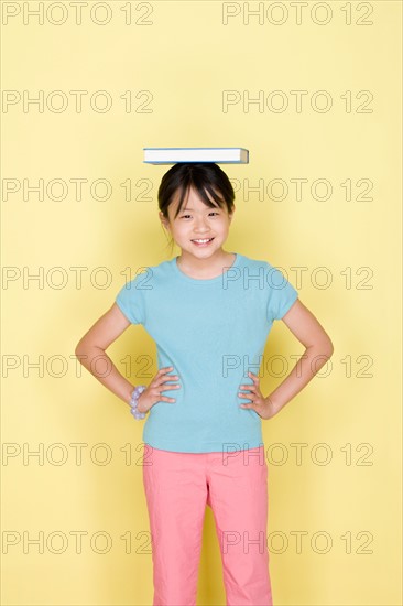 Studio portrait of teenage (16-17) girl balancing book on head. Photo : Rob Lewine