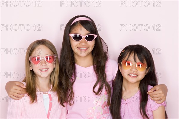 Studio portrait of three teenage (16-17) girls wearing sunglasses. Photo : Rob Lewine