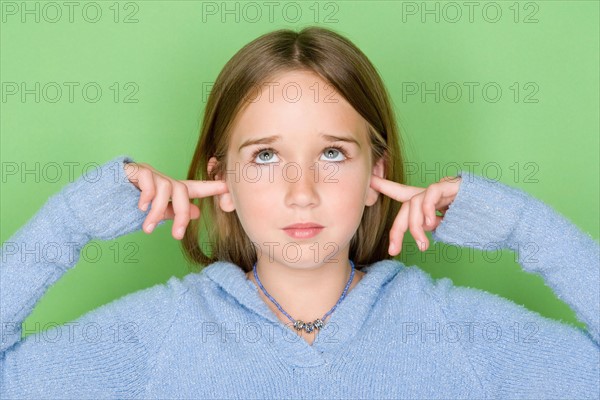 Studio shot portrait of teenage girl with fingers in ears, head and shoulders. Photo : Rob Lewine