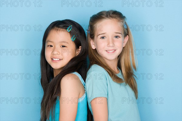 Studio shot portrait of two teenage girls standing back to back, head and shoulders. Photo : Rob Lewine