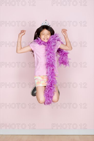 Studio shot portrait of jumping teenage girl in diadem and feather boa shawl, full length. Photo : Rob Lewine