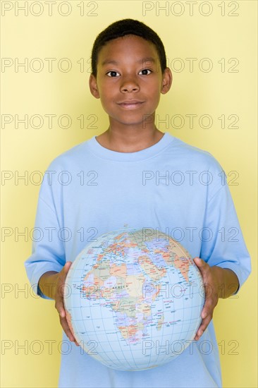 Studio shot portrait of young man holding globe ball, waist up. Photo : Rob Lewine