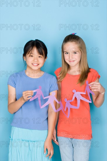 Studio shot portrait of two teenage girls holding paper chain, three quarter length. Photo : Rob Lewine